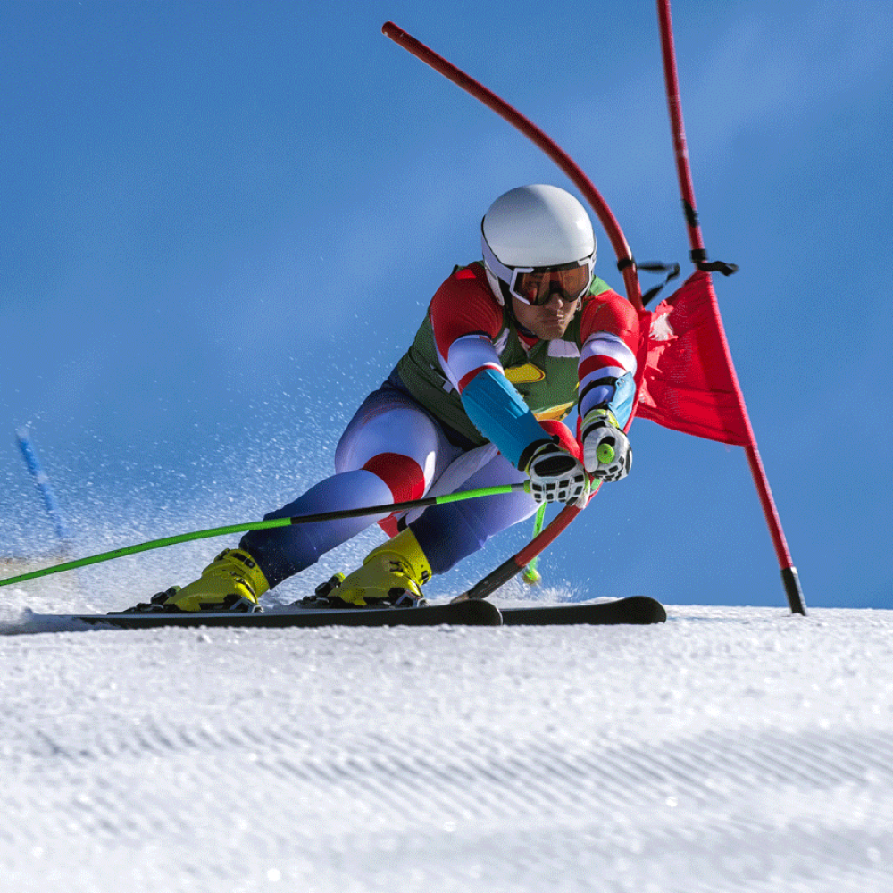 Young man compeeting at giant slalom race, bending the red gate, against the blue sky